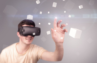 Young impressed man wearing virtual reality goggles with grey cubes around him 