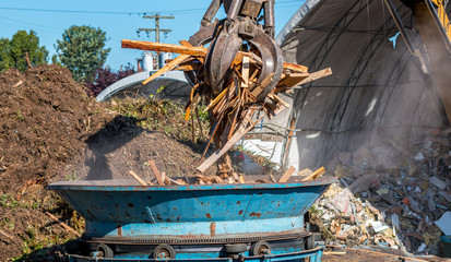 A machine grapple dopes construction waste into grinder to be recycled into wood chips. 