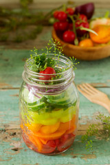 Salad of vegetables with herbs in a glass jar and fresh vegetables on a table.