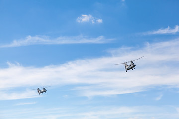 Fototapeta na wymiar Two Helicopters flying against a blue sky with white clouds and copyspace