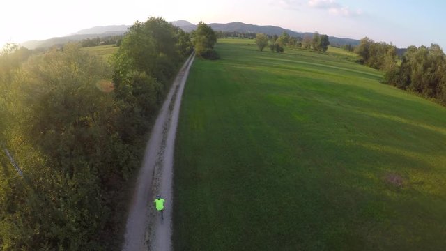 Woman cycling on a country road at sunset. Aerial footage