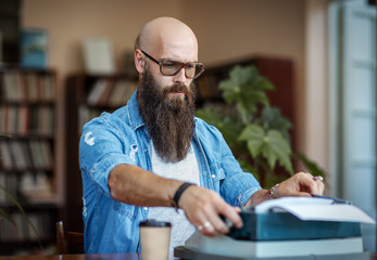 Bearded stylish writer typing on typewriter - Powered by Adobe