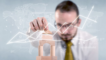 Young handsome businessman using wooden building blocks with data and calculations behind him