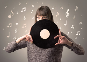 Young lady holding vinyl record on a brown background with musical notes behind her