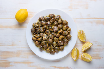 Tasty fried snails with lemon in white plate on white wooden background. © Paopano