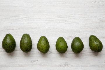 Whole avocados on white wooden surface, top view. Overhead, from above. Copy space.