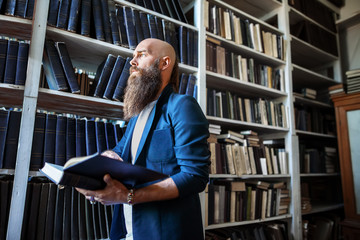 Stylish bearded man with book in library