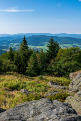 Fototapeta na wymiar View from top of a mountain in the valley with clouds on the sky and mountains on the background and stones and trees in front of in the bavarian forest