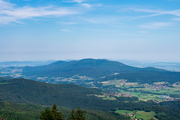 View from top of a mountain in the valley with clouds on the sky and mountains on the background and stones and trees in front of in the bavarian forest