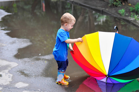 The little boy in colored rubber boots playing with his rainbow umbrella in puddles.