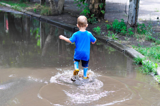 Two-year-old baby boy runs through puddles in rubber boots
