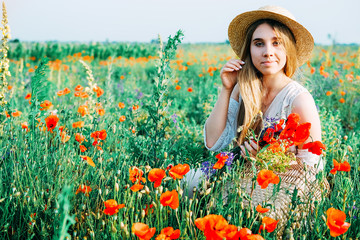 Young countryside girl sitting in the field of poppies