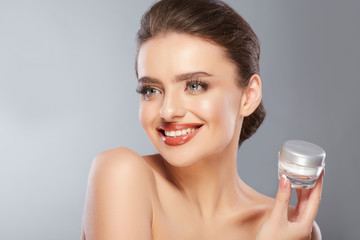 Beauty concept, Beauty Woman Face. Closeup Of Beautiful Young Female Model With Fresh Skin Holding Cream Bottle In Hand. Portrait Of Sexy Girl Applying Cosmetic Product. Skincare Concept.