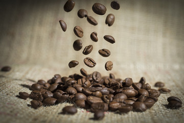 Closeup falling coffee beans on a hessian background.