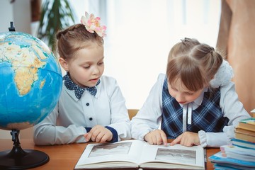 Two schoolgirls sit at a desk with a globe
