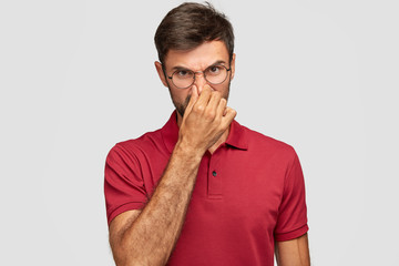 Dissatisfied man closes nose, feels stench, frowns face, feels about bad smell coming from kitchen,...
