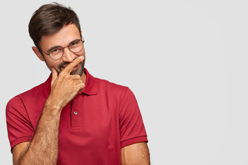 Positive funny youngster laughs happily, covers mouth, has joyful expression, tries to conceal his...