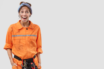 Photo of exultant happy female industrial worker looks positively, doesnt expect to recieve bonus for diligent work from foreman, stands against white background with copy space on right side