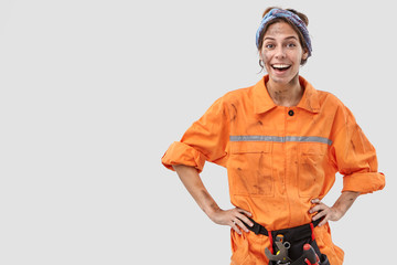 Horizontal shot of positive professional skilled experienced female service worker, has tool belt,...