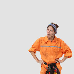 Vertical shot of discontent hopeless tired emotive labour worker looks upwards, has to daub plaster on ceiling, repairs something in room, isolated over white background with blank space aside and up