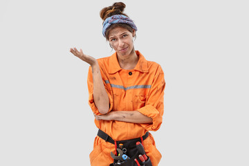 Pessimistic discontent hopeless plumber regrets something, wears orange dirty uniform, makes regreting gesture, poses alone against white background. Crestfallen exasperate female carpenter.