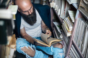 Stylish hipster man reading book sitting on floor in bookstore