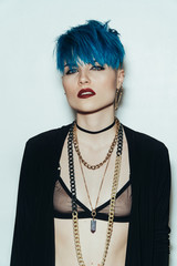 fashion photography of a girl with blue hair on a white background looking straight into the camera. Thick yellow chain and bijouterieher on her neck. Professional model posing in studio