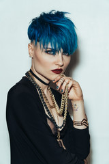 fashion photography of a girl with blue hair on a white background looking directly at the camera. Thick yellow chain and bijouterieher on her neck. Professional model posing in studio