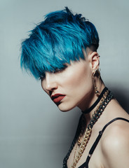 fashion photography of a girl with blue hair on a white background. Thick yellow chain and bijouterieher on her neck. Professional model posing in studio.
