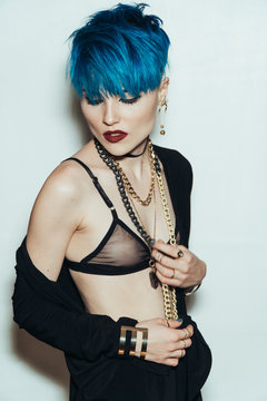 fashion photography of a girl with blue hair on a white background. Thick yellow chain and bijouterieher on her neck. Professional model posing in studio.