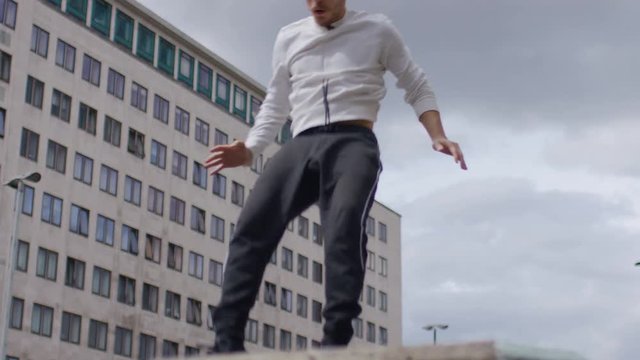 Young man doing a parkour front flip in the city, in slow motion  