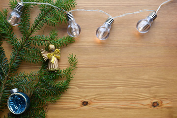 Christmas and New Year composition on a wooden background. A branch of a Christmas tree with an electric garland and Christmas decorations. Concept for a greeting card, poster. Place to insert text.