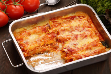 Caneloni stuffed with meat and melted cheese in metal bowl over grunge wood background