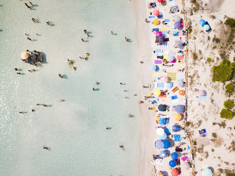 Aerial view of a white beach full of colored beach umbrellas and relaxed people swimming on a clear sea. Cala Brandinchi, Sardinia, Italy.