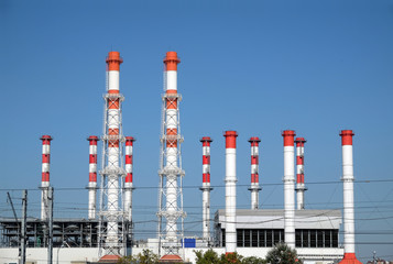 City landscape with power station building with many high red and white industrial pipes over clear cloudless blue sky on sunny day front view