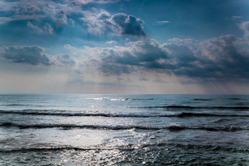 Ocean view with dramatic clouds above it and sun rays visible.