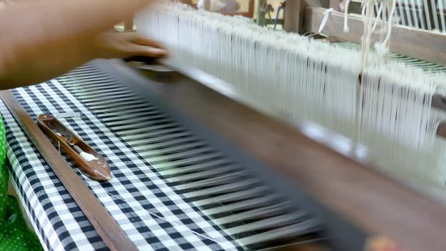 Close up woman is weaving Thai silk fabric by traditional weave machine in textile industry. (4K Video)
