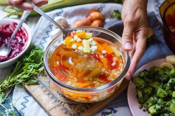Woman hands stirs vegetables broth soup with corn, carrot, red pepper, potato, pumpkin, onion, cabbage, spices and herbs, Vegan vegetarian healthy food lunch or dinner