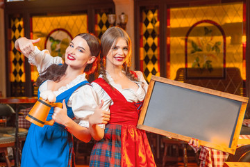 Young girls with wooden beer mugs and a wooden tablet for text in hands at the Oktoberfest festival.