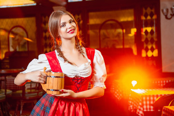 Young beautiful girl with a wooden mug of beer in hands at a party Oktoberfest.