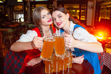 Young beautiful girls clink glasses with beer at the Oktoberfest festival.