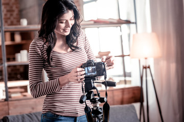 Advanced gadget. Joyful dark-haired woman fixing her camera while making a video for her blog