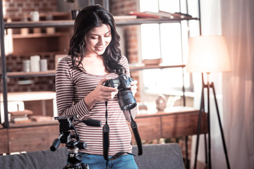 Cheerfulness. Joyful dark-haired woman holding her advanced camera and smiling