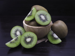 Slice of fresh juicy delicious and healthy kiwi fruits on wooden bowl, on black wood background.