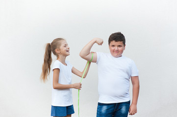 pretty laughing thin little girl measuring cute fat boy biceps muscle with tape