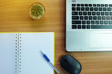 notebook with empty space and a pen,with laptop computer and wireless mouse on the desk wooden with cactus. topview