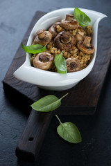 Bowl of pasta with mushrooms and green basil leaves on a black wooden serving board, studio shot