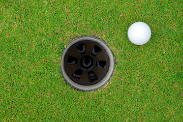 Golf ball and golf hole on green grass.
