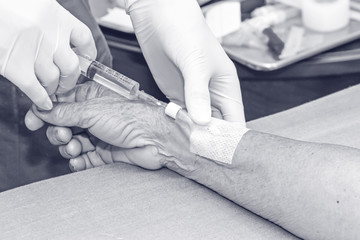 Doctor push syringe in heparin plug hand of patient,processec in black and white tone.
