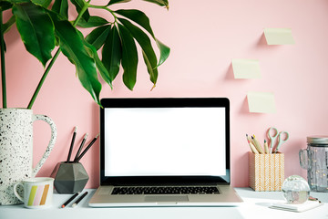 Stylish and creative desk with laptop mock up screen, tropical leaf, office accessories and memo stick. Pink background wall. Design home office interior. 
